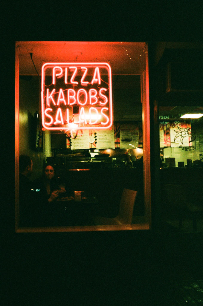the outside of a pizza shop with a neon sign