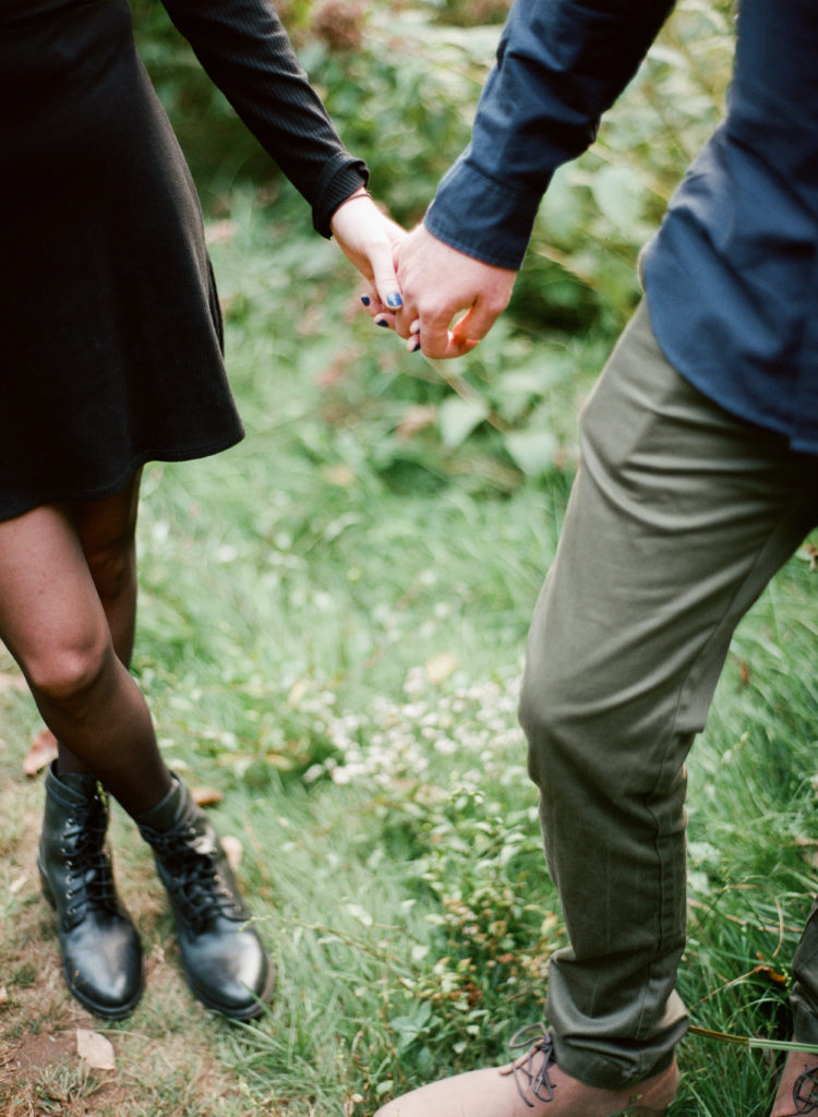 a close up of a couple holding hands while standing in a field of grass