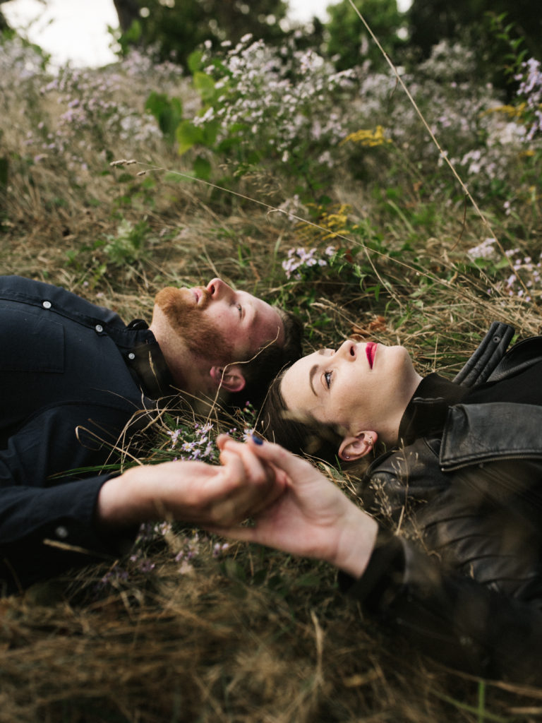 a couple holding hands while laying down in a field of grass