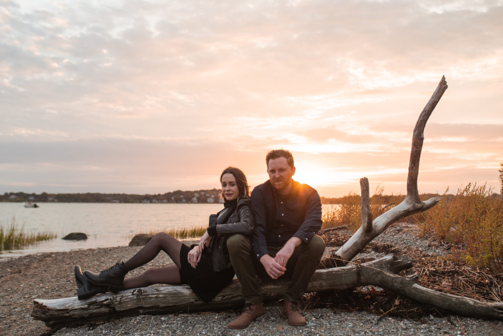 a couple sitting on a piece of driftwood at sunset